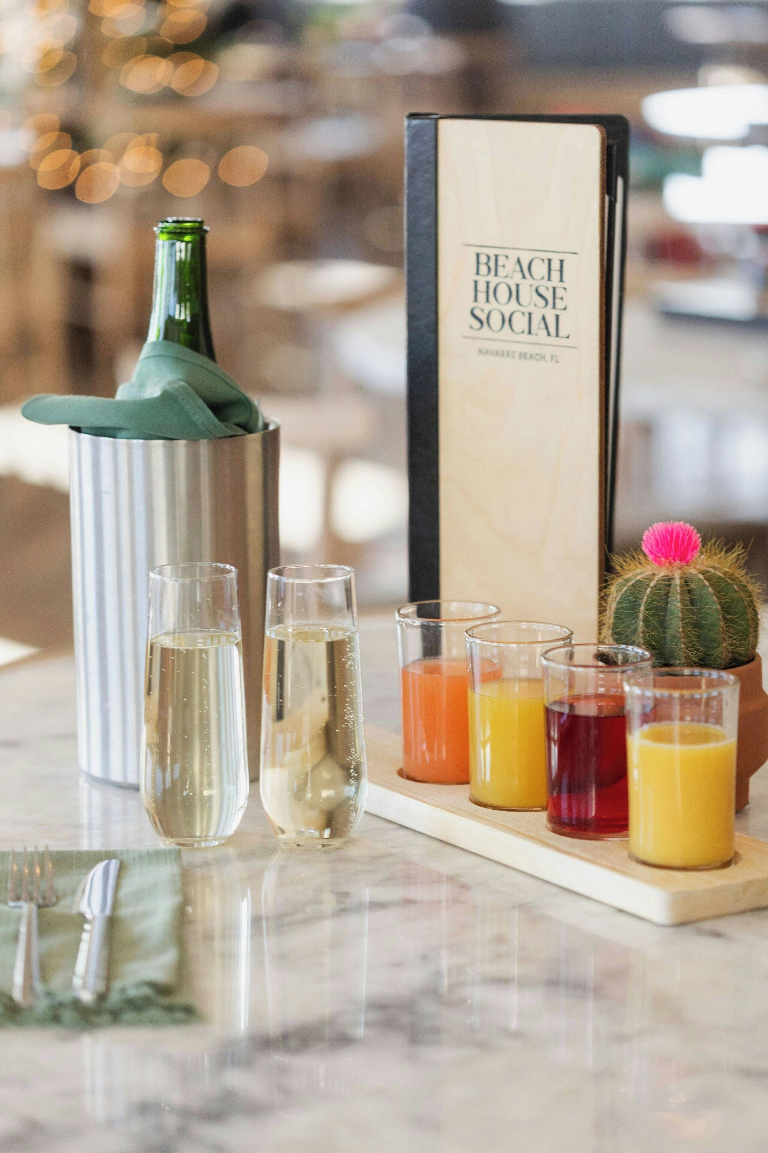 A table with a bottle of champagne, two glasses of champagne, and a tray with various drinks and a cactus.