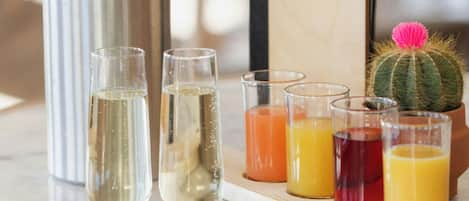 A table with a bottle of champagne, two glasses of champagne, and a tray with various drinks and a cactus.