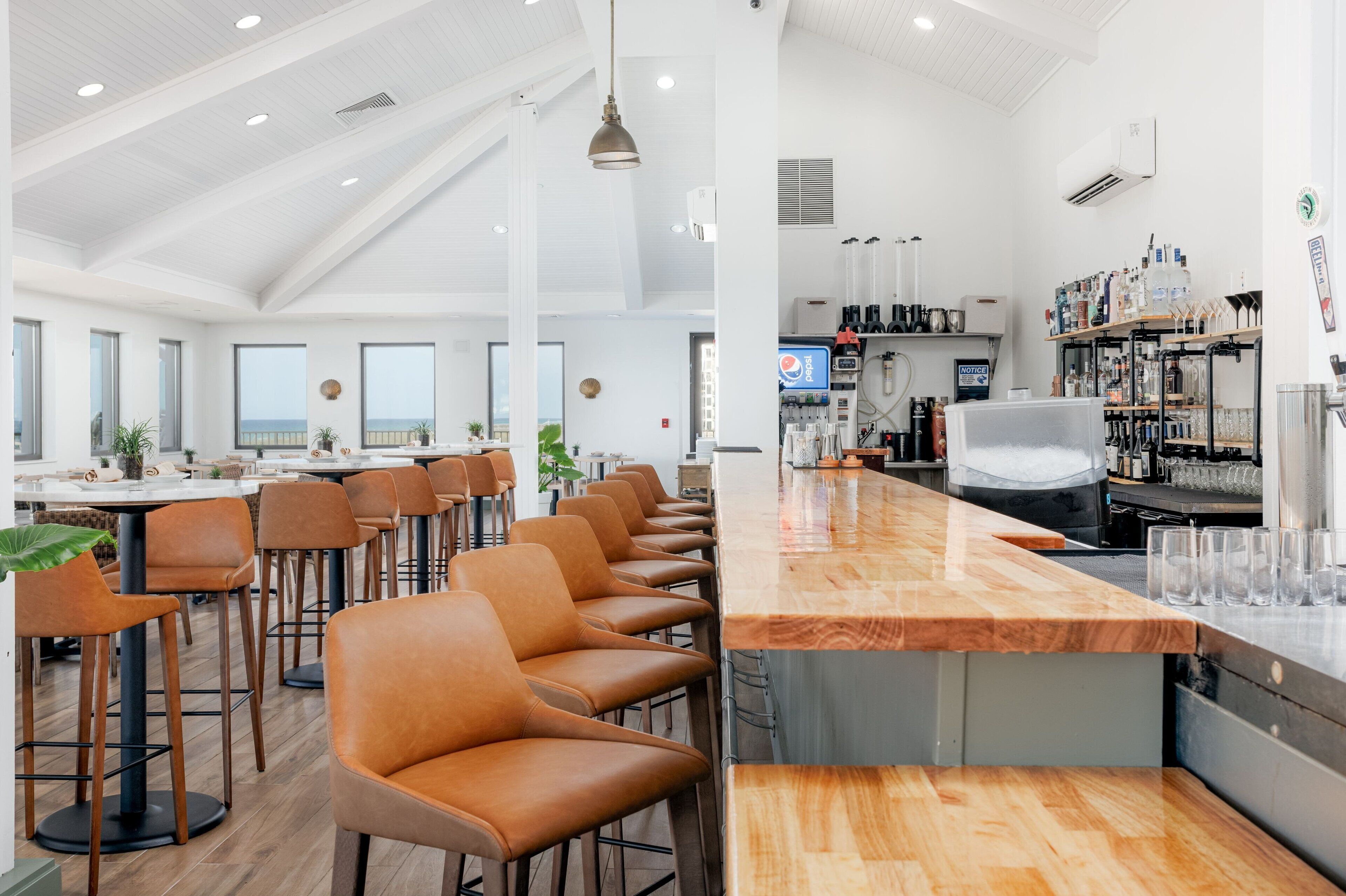 A modern bar area with a long counter, bar stools, and a variety of bottles and glasses.