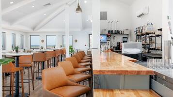 A modern bar area with a long counter, bar stools, and a variety of bottles and glasses.