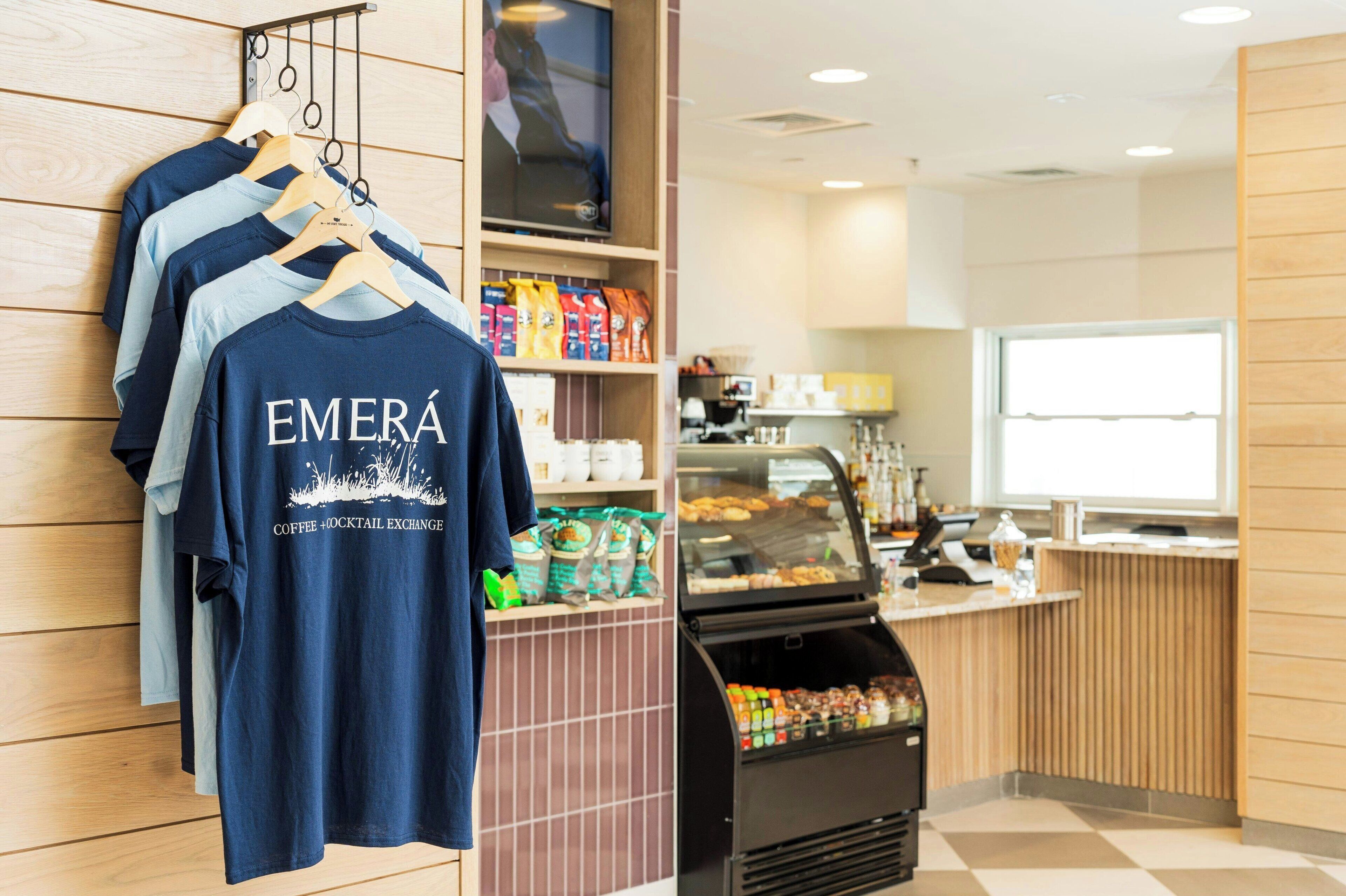 A coffee shop interior with a counter, a display of coffee bags, and a hanging rack with t-shirts.