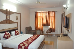 A hotel room with a bed, a desk, a chair, a television, and a ceiling fan.