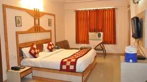 A hotel room with a wooden bed, a nightstand, a chair, an air conditioning unit, and a television.