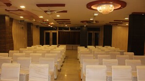 A conference room with rows of white chairs, a chandelier, ceiling fans, and a wooden panel wall.