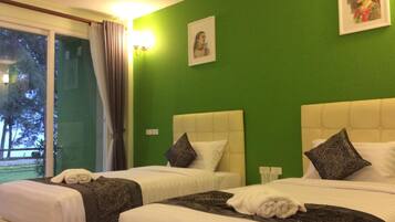 Habitación de hotel con dos camas, paredes verdes y un ventanal grande con cortinas.