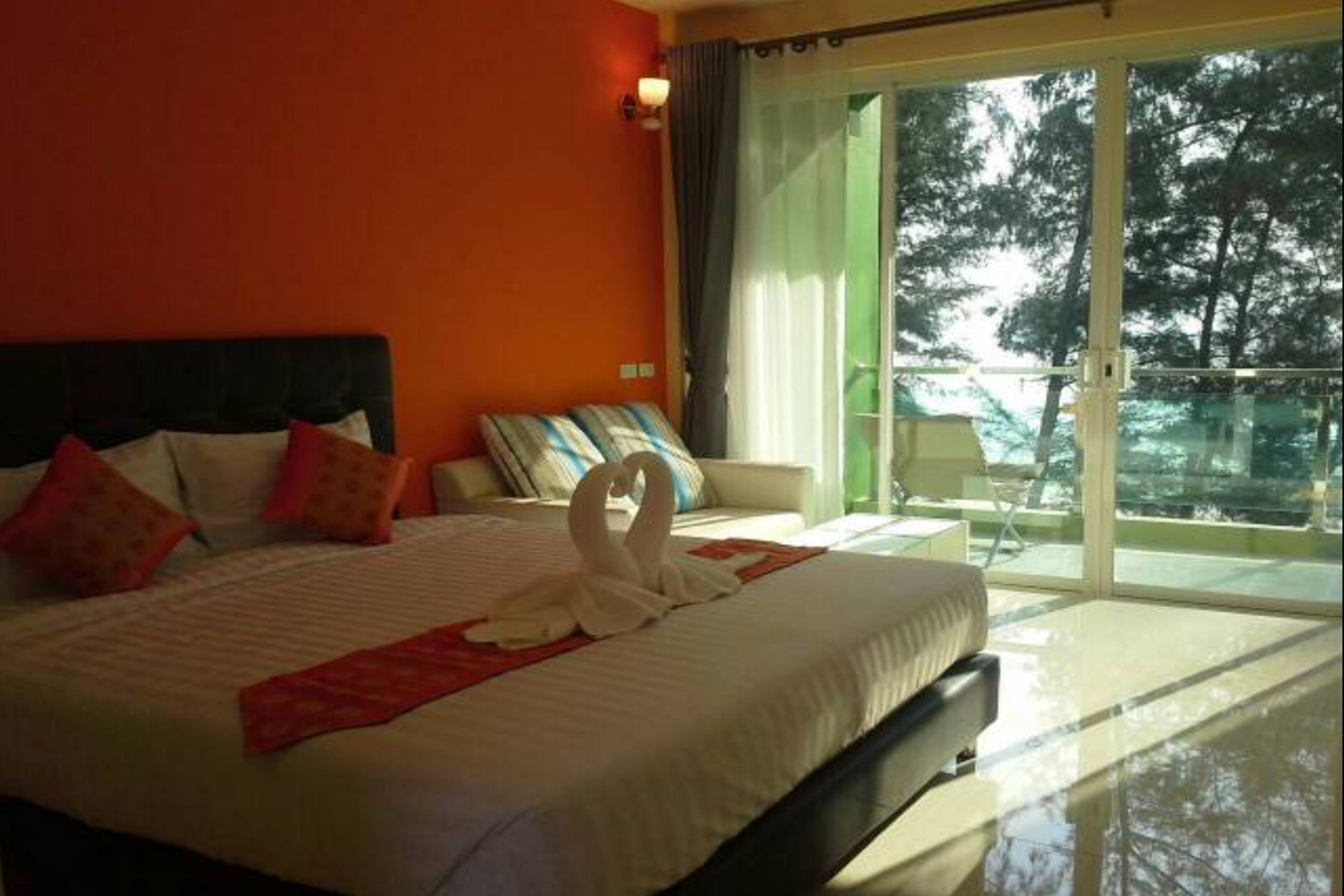 A hotel room with a large bed, a sofa, and a balcony with a view of trees.