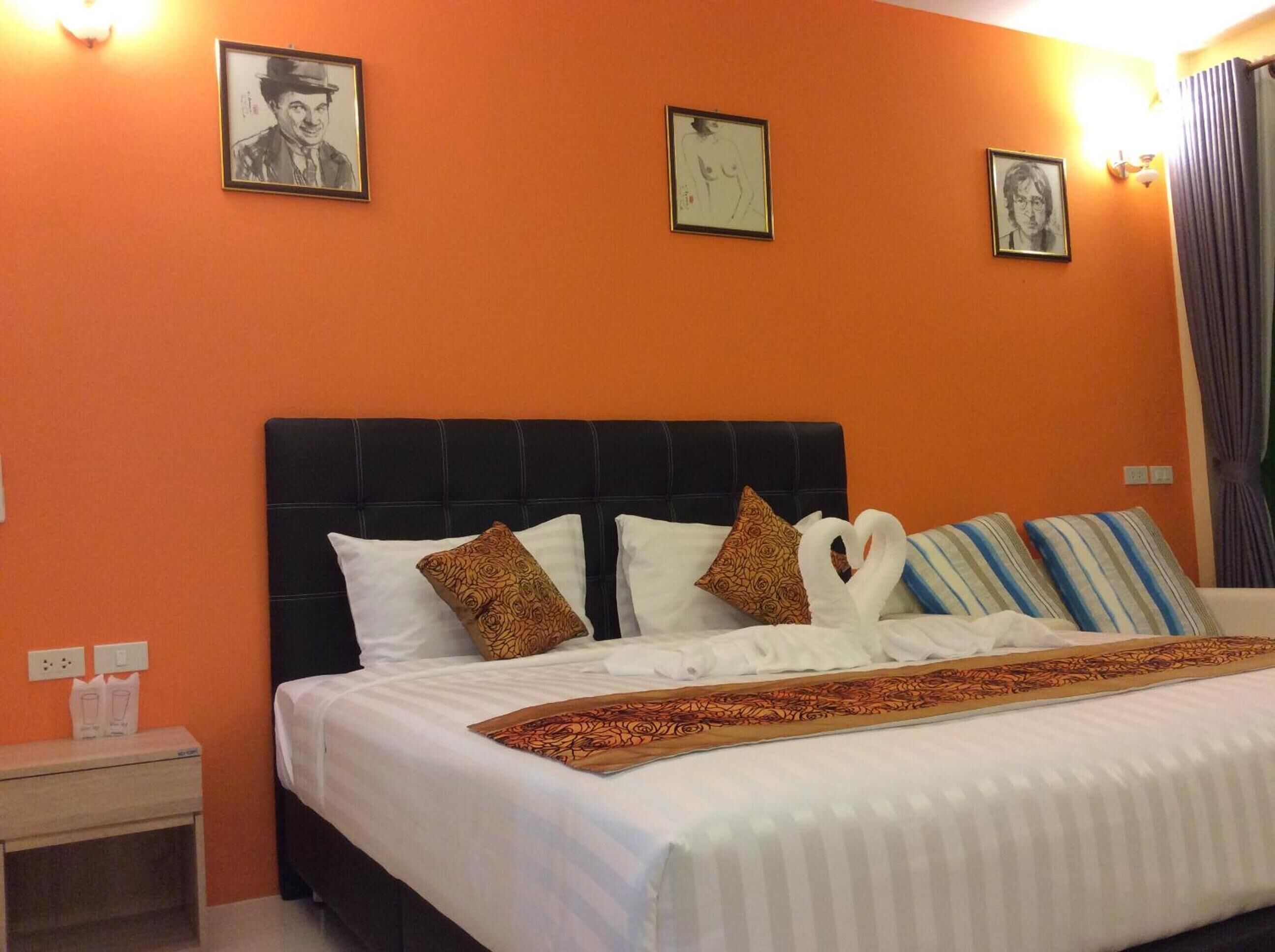 Habitación de hotel con pared naranja, cabecera negra y cama con ropa blanca y almohadas estampadas.
