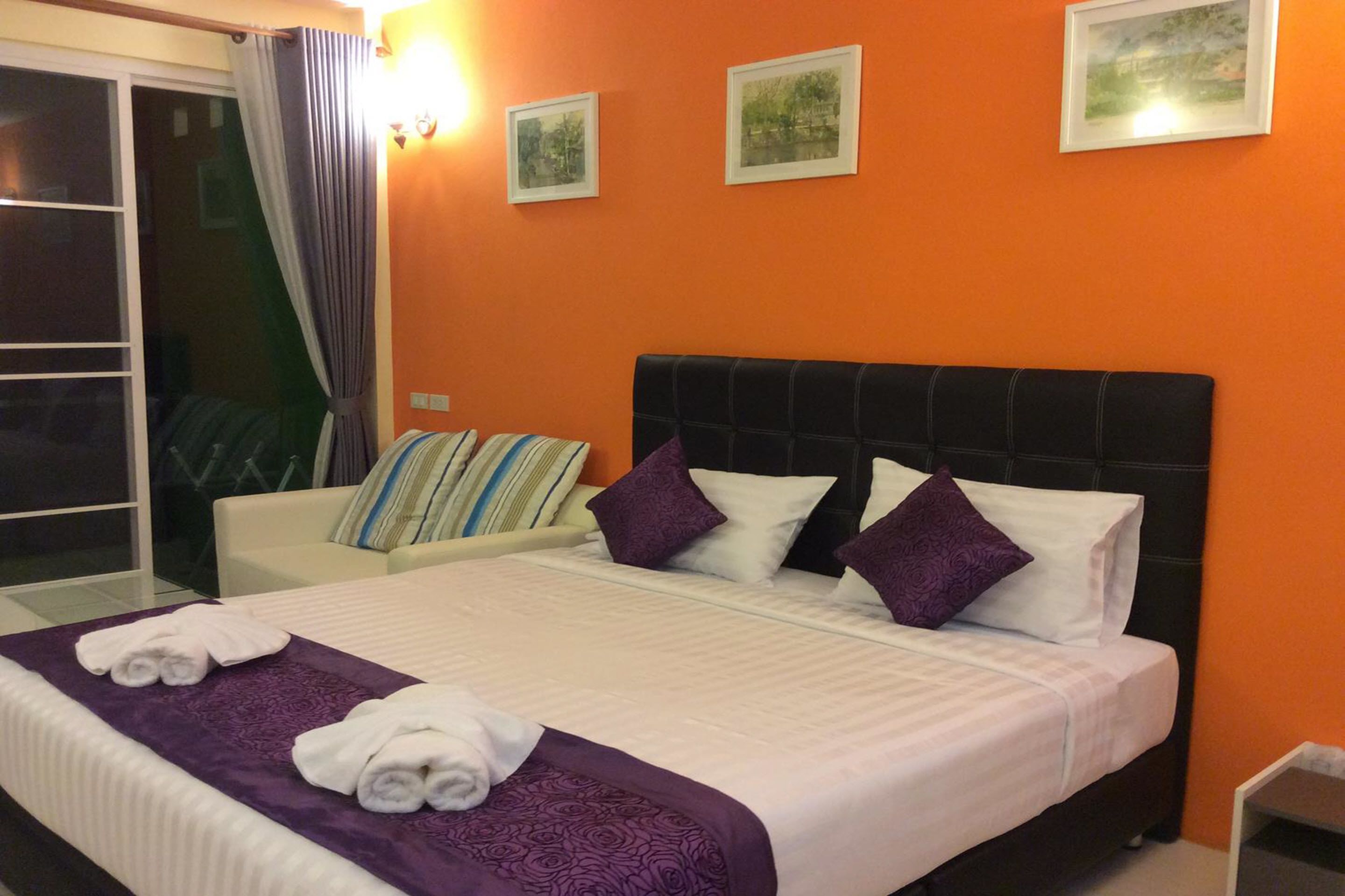 A hotel room with a large bed, a white sofa, and a balcony with curtains.