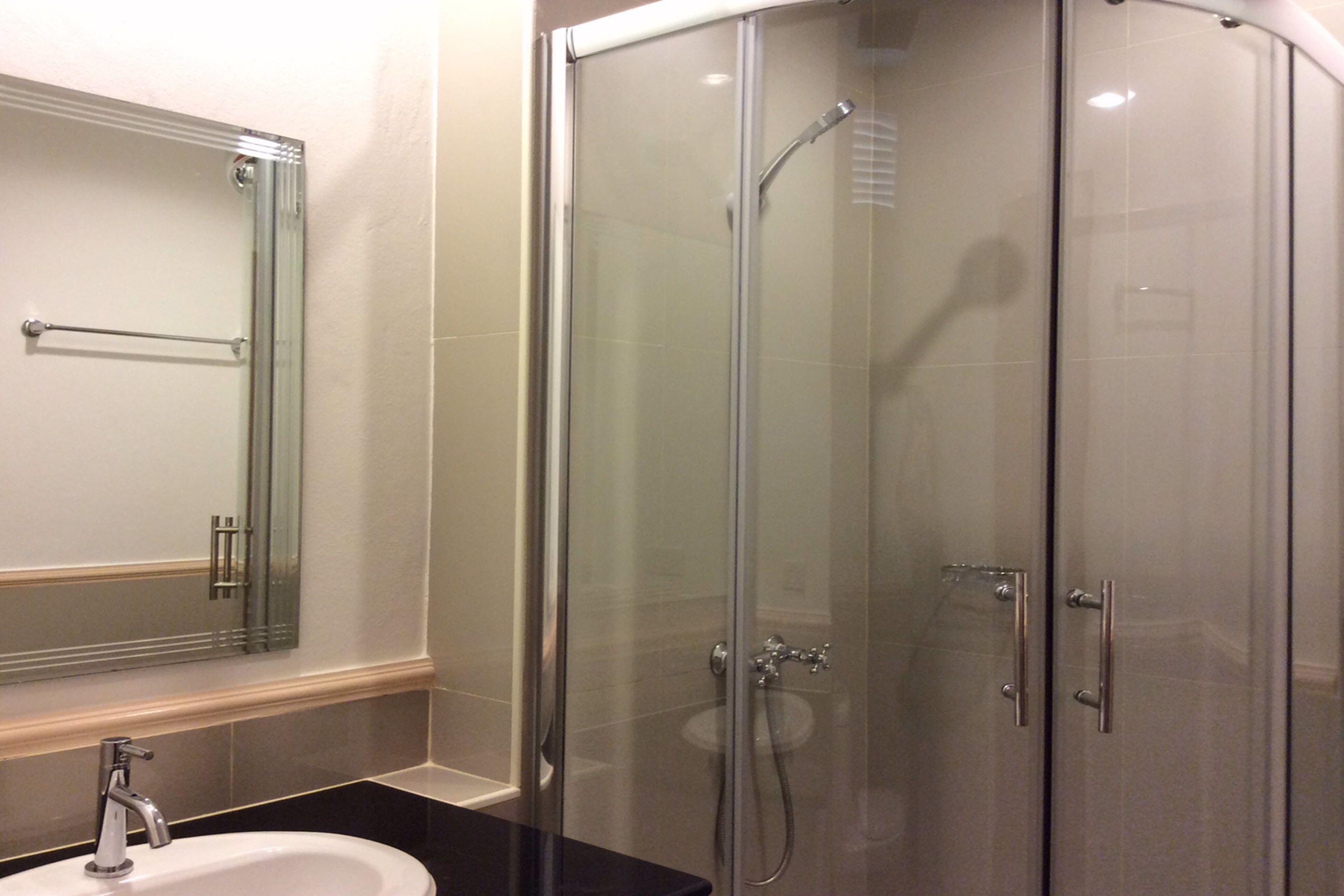A modern bathroom with a glass-enclosed shower, a sink with a mirror above it, and a towel rack.