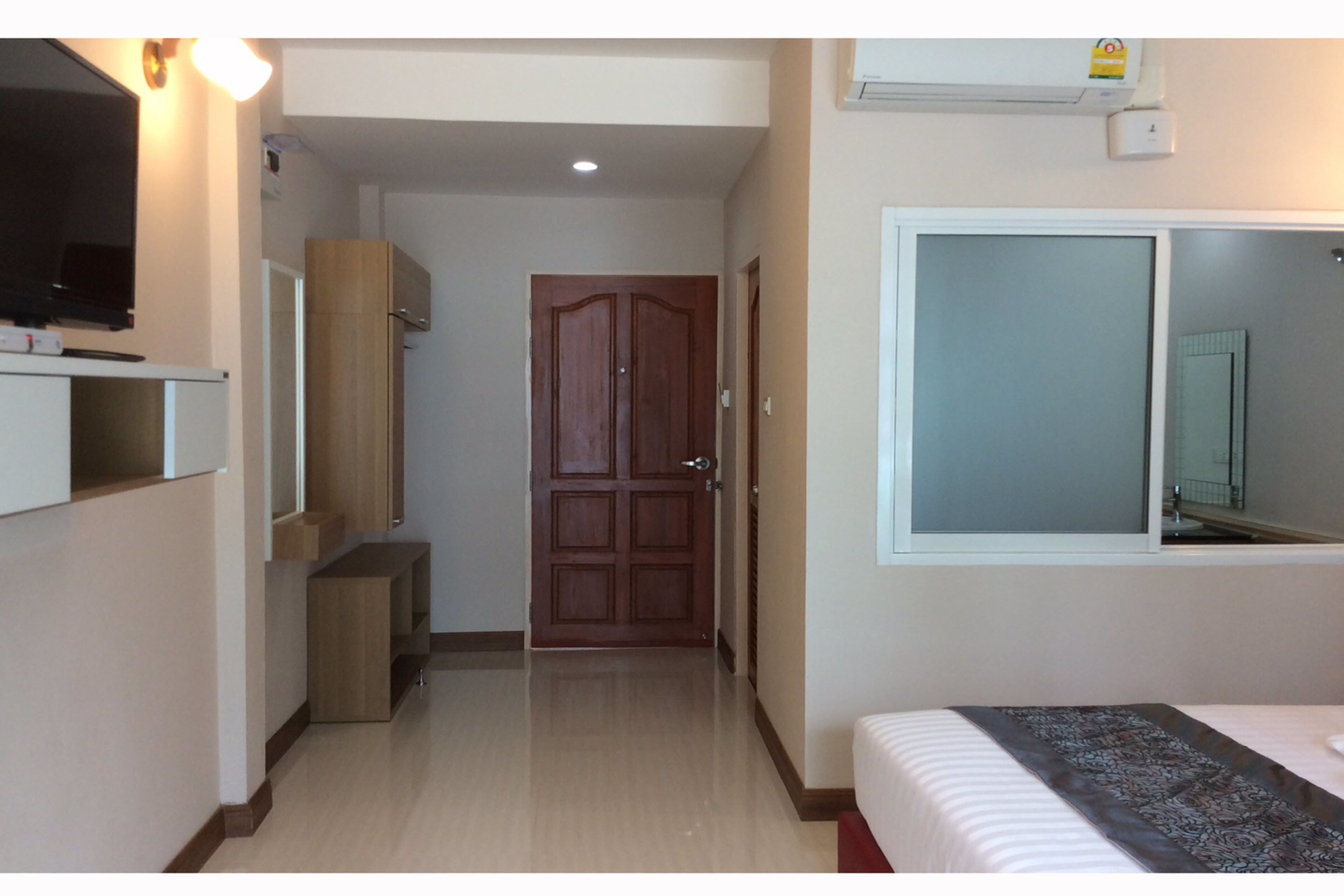 A hotel room with a bed, a television, a wardrobe, a mirror, and a door leading to another room.