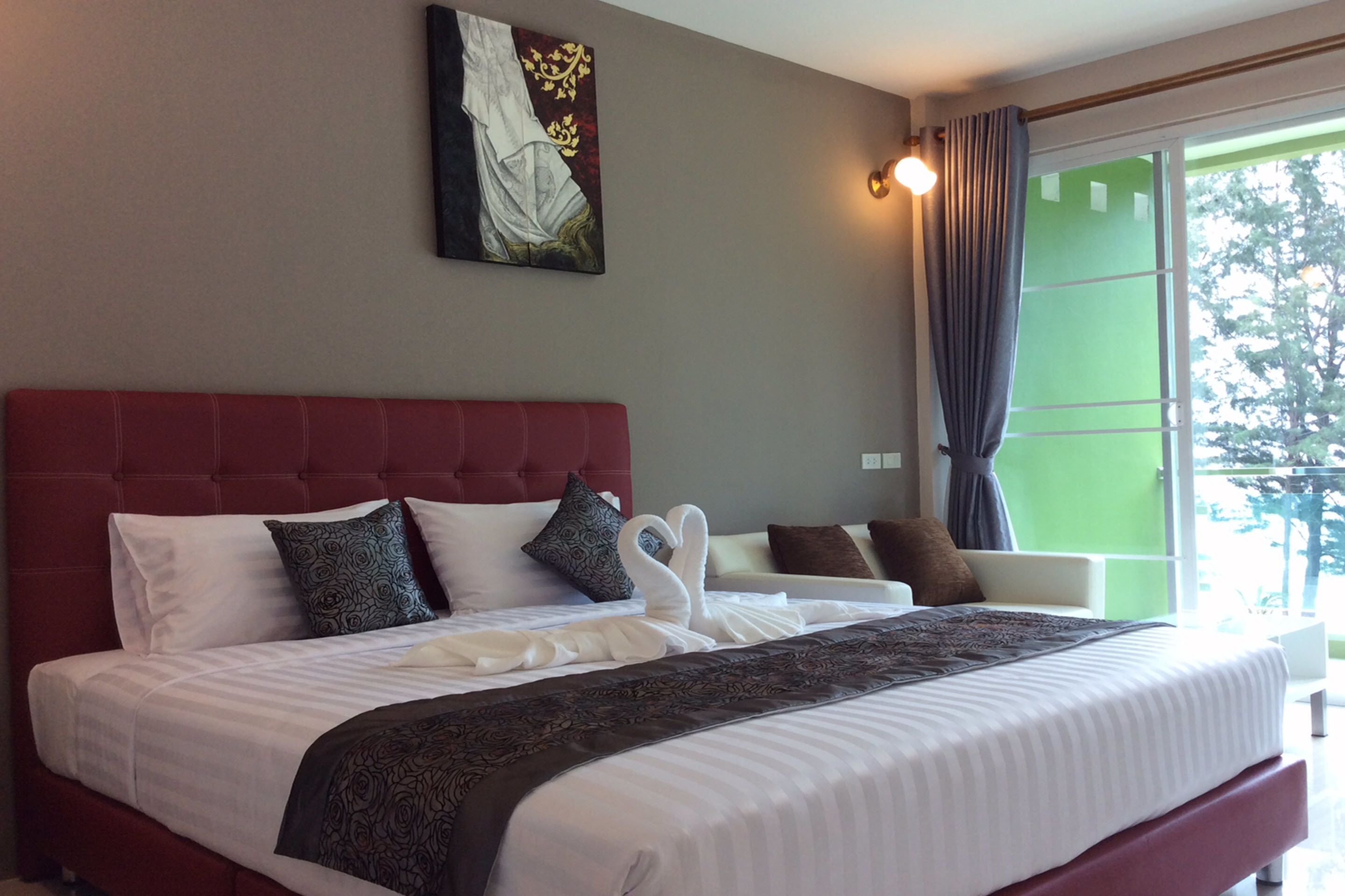 A hotel room with a large bed, a red headboard, and a painting on the wall.