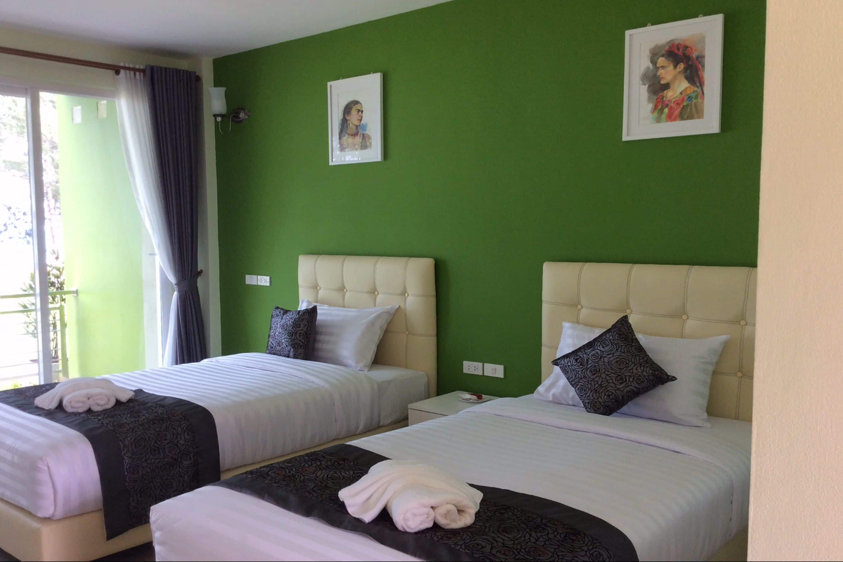 A hotel room with two beds, green walls, and two framed pictures on the wall.