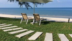 Un área de estar junto a la playa con dos sillones reclinables y un gran parasol, con vista al océano.