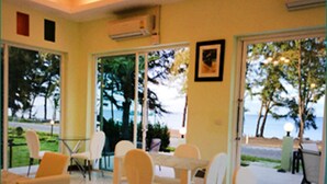 Un restaurante con vistas al mar, que cuenta con una disposición de mesas y sillas, y un puerta de cristal que da al exterior.
