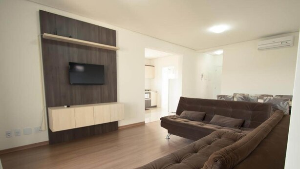 A modern living room with a brown sofa, a mounted TV, and a wooden cabinet. - Residencial Scheifler (Gramado)