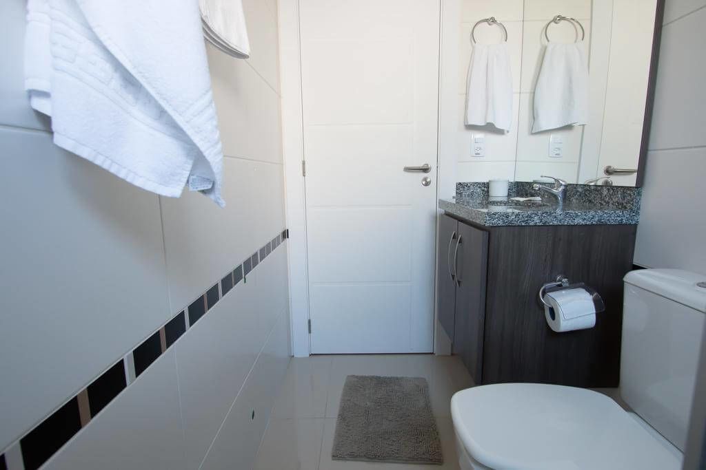 Un baño con inodoro blanco, lavamanos con encimera de mármol y toallero con toallas blancas.