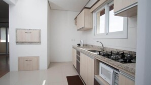 A modern kitchen with light wood cabinets, a granite countertop, a gas stove, and a window above the sink. - Residencial Scheifler (Gramado)
