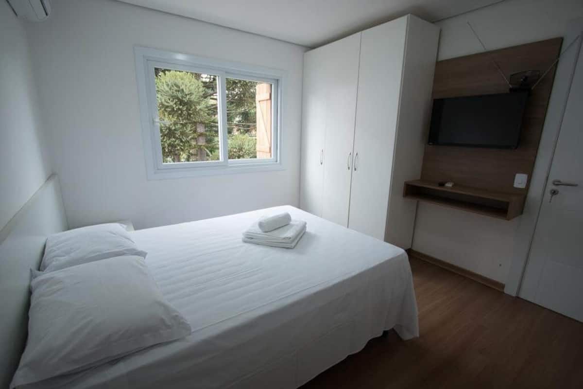 Une chambre à coucher avec un lit, une fenêtre, un téléviseur fixé au mur et une armoire.