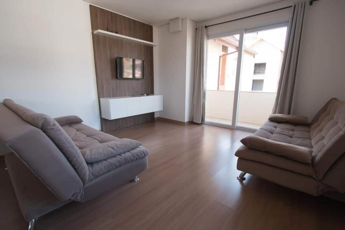 Un salon moderne avec un canapé, un téléviseur à écran plat fixé sur un panneau en bois et une porte-fenêtre coulissante donnant sur un balcon.