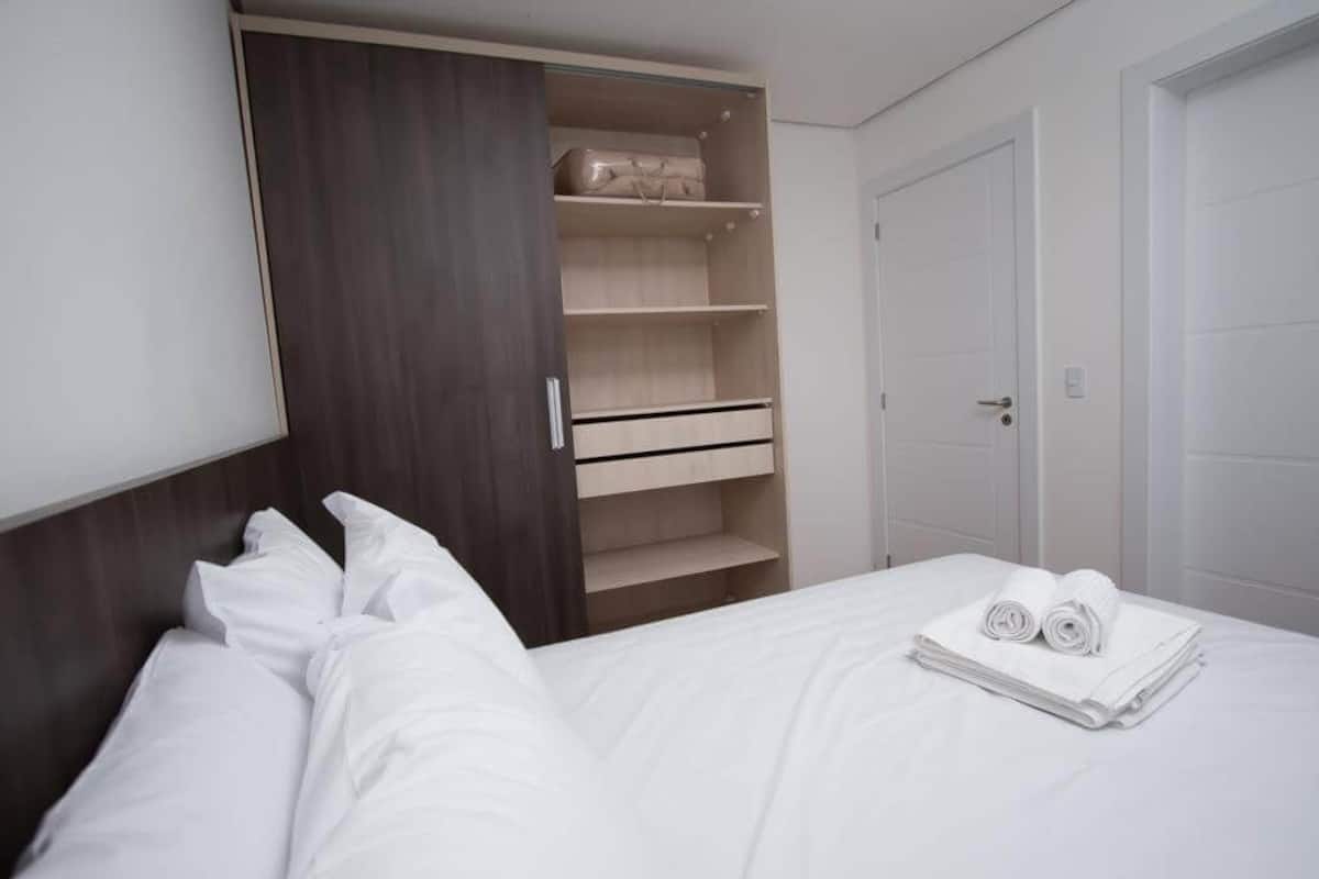 Une chambre d’hôtel avec un lit, une armoire dotée de plusieurs étagères et une porte.