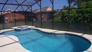 Une piscine avec un jacuzzi, entourée d’une clôture en métal, et des maisons en arrière-plan.