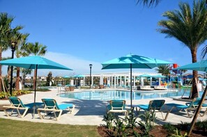 Ein Poolbereich mit Liegestühlen und Sonnenschirmen, umgeben von Palmen und einem Gebäude mit Wasserrutsche.