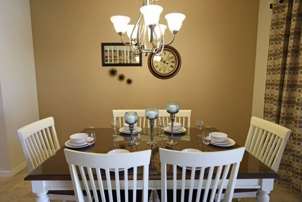 A dining table with white chairs, a chandelier, and a clock on the wall.