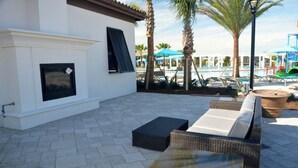 Une terrasse extérieure avec des meubles en osier, une cheminée et, au fond, un espace piscine.