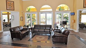 A spacious lobby with a brown leather sofa set, a patterned rug, and large arched windows with plants. - 211 Terra Verde House 7 Bedroom by Florida Star (Kissimmee)