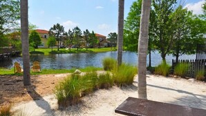 A lakeside view with a sandy beach, palm trees, and a bench. - 211 Terra Verde House 7 Bedroom by Florida Star (Kissimmee)