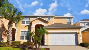 A two-story house with a garage, a front entrance, and a well-maintained lawn with palm trees. - 211 Terra Verde House 7 Bedroom by Florida Star (Kissimmee)