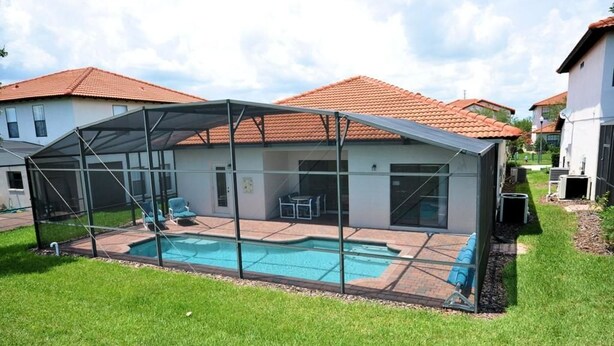 A covered outdoor swimming pool with a glass enclosure, surrounded by a lawn and adjacent houses. - 211 High Grove House 4 Bedroom by Florida Star (Clermont)