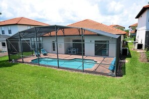 A covered outdoor swimming pool with a glass enclosure, surrounded by a lawn and adjacent houses. - 211 High Grove House 4 Bedroom by Florida Star (Clermont)