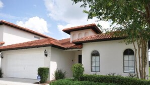 A single-story house with a white exterior, a red-tiled roof, and a garage. - 211 High Grove House 4 Bedroom by Florida Star (Clermont)
