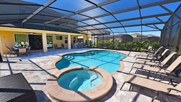 Un área de piscina al aire libre con un jacuzzi, sillas de descanso y un porche cubierto.