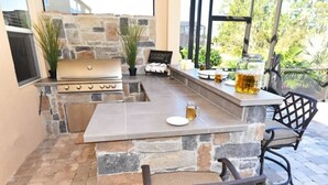 An outdoor kitchen area with a stone countertop, a grill, and bar seating. - 216 Watersong House 7 Bedroom by Florida Star (Davenport)