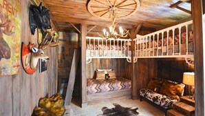 A rustic cabin interior with wooden walls, a chandelier, a loft bed, a sofa, and a dining table. - 216 Watersong House 7 Bedroom by Florida Star (Davenport)