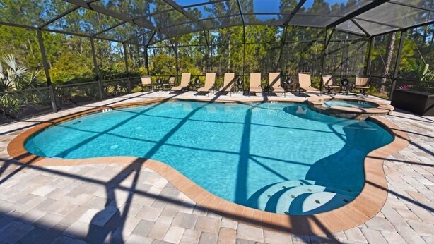 A covered outdoor swimming pool with lounge chairs and a wooden deck. - 216 Watersong House 7 Bedroom by Florida Star (Davenport)