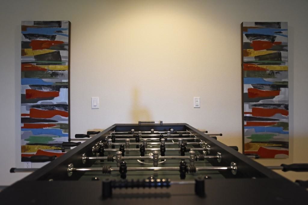 Una mesa de fútbolín en una habitación con paredes lisas y dos cuadros abstractos a cada lado.