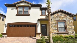 A two-story house with a stone facade, a brown garage door, and a well-maintained front yard with a palm tree. - 2167 Windsor at Westside House 8 Bedroom by Florida Star (Kissimmee)