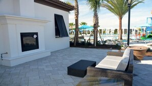 An outdoor patio with wicker furniture, a fireplace, and a pool area in the background. - 2167 Windsor at Westside House 8 Bedroom by Florida Star (Kissimmee)