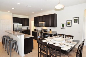 A modern kitchen with dark cabinets, a central island, and a dining area set for six.