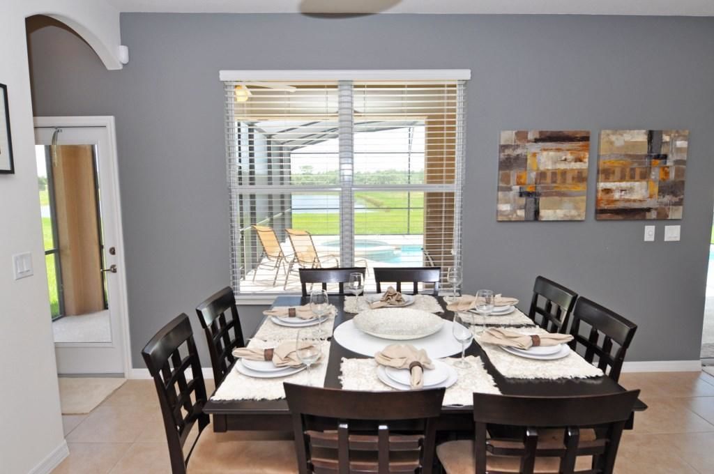 A dining area with a table set for six, a view of a pool through large windows, and abstract art on the wall.