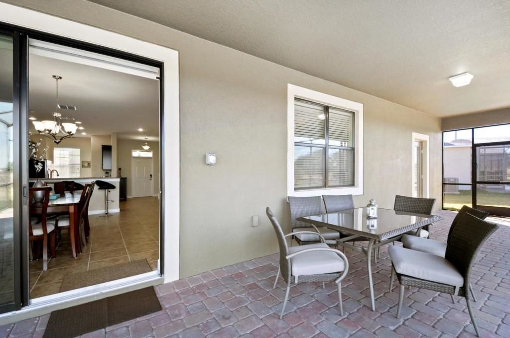 A patio area with a table and chairs, a kitchen visible through a glass door, and a large window with blinds.