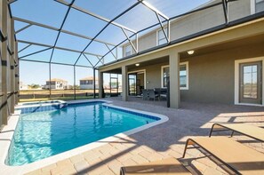 Una piscina interior con paredes de vidrio transparente, suelo de baldosas y sillones de descanso.