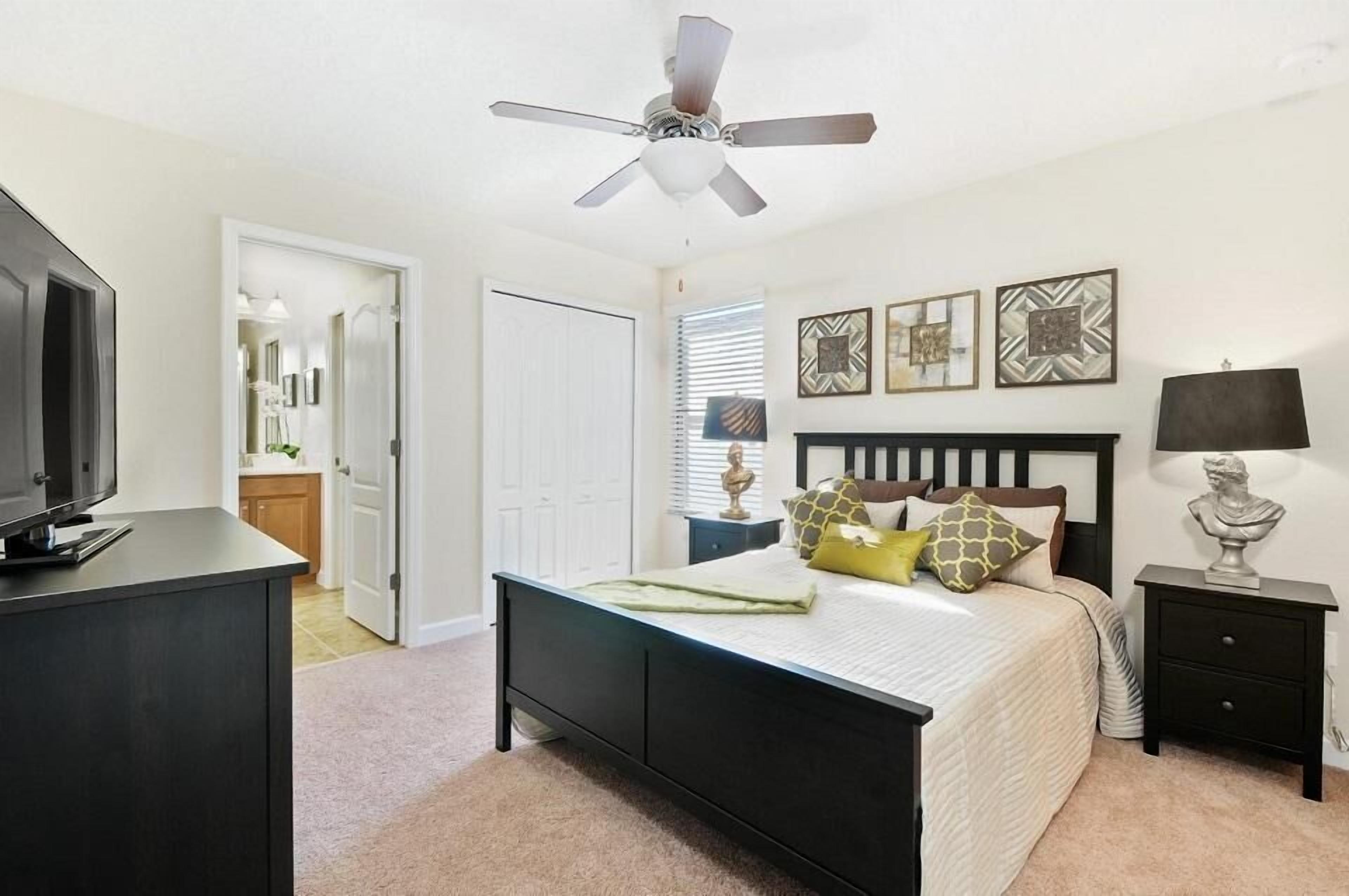 A bedroom with a bed, a ceiling fan, a nightstand, a lamp, and a TV.