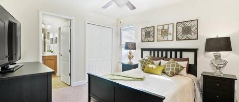 A bedroom with a bed, a ceiling fan, a nightstand, a lamp, and a TV.