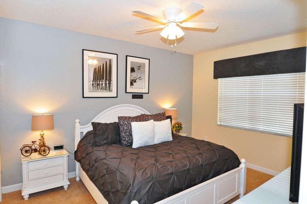 A bedroom with a bed, two bedside tables, a ceiling fan, and framed pictures on the wall.