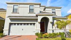 A two-story house with a garage, a red door, and a small garden with plants and a palm tree. - 2329 Providence House 8 Bedroom by Florida Star (Davenport)