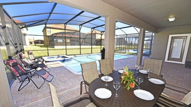 An outdoor patio with a covered dining area, a pool, and lounge chairs. - 2341 Providence House 6 Bedroom by Florida Star (Davenport)